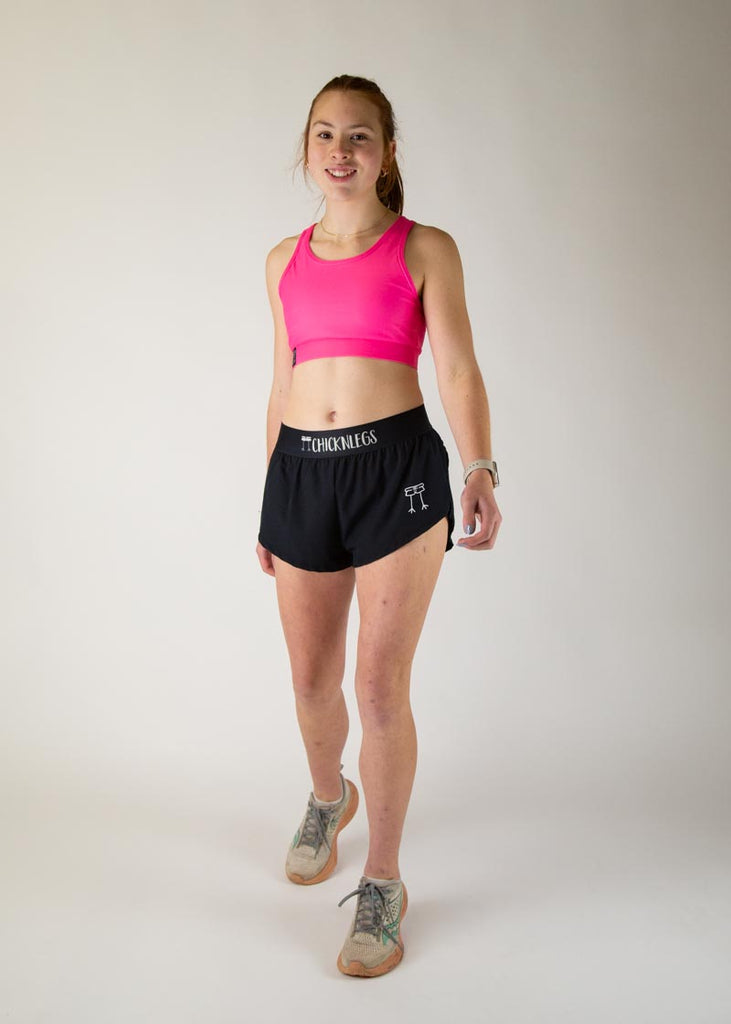 The model is a runner who is wearing Chicknlegs in the women's OG sports bra in the neon pink design, facing front while posing in a walking stance. A full body is shown of the model.