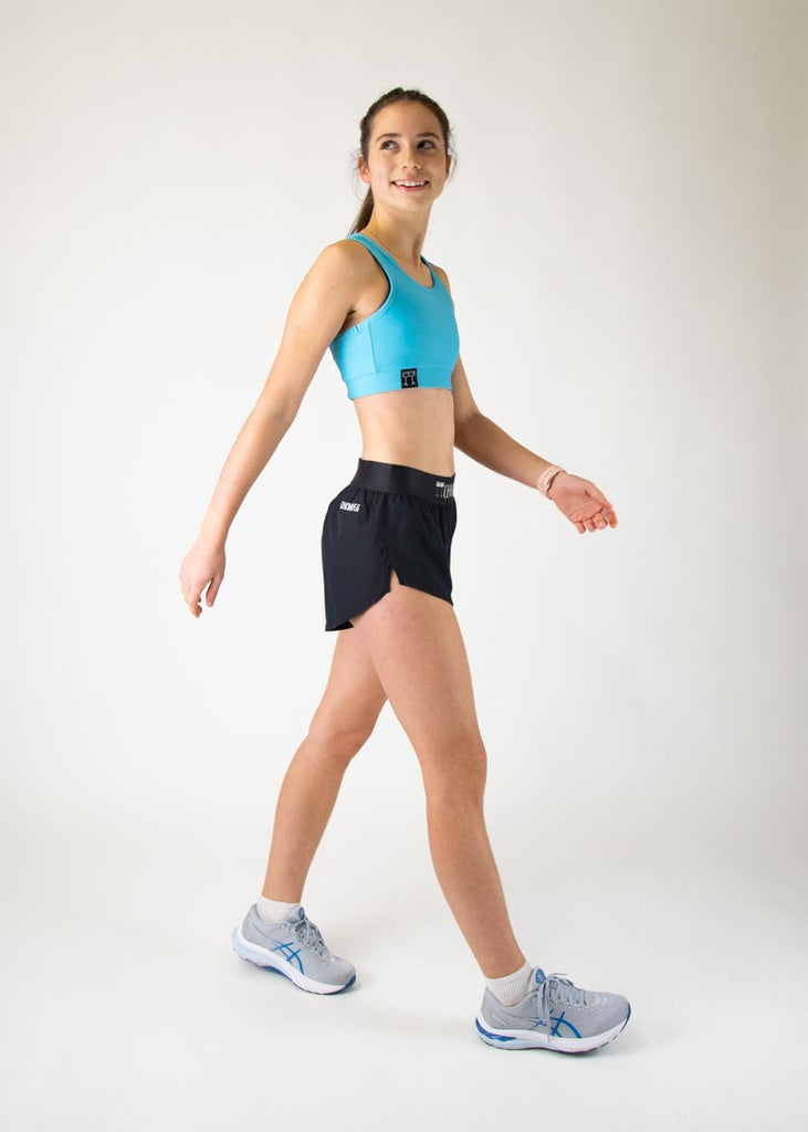 The model is a runner who is wearing Chicknlegs in the women's OG sports bra in the sky blue design, facing front while in a walking stance. A full body is shown in this image of the model.