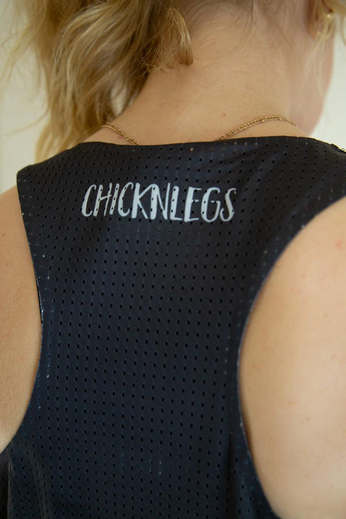 Runner is wearing ChicknLegs in the women's performance singlet in the solid black design. A close up of the back of the singlet is shown to show the breathable material.