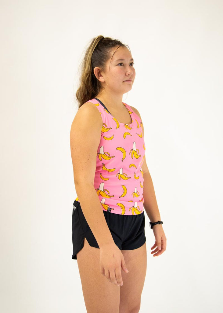The model is a runner who is wearing Chicknlegs women's performance singlet in the pink banana design, facing right.