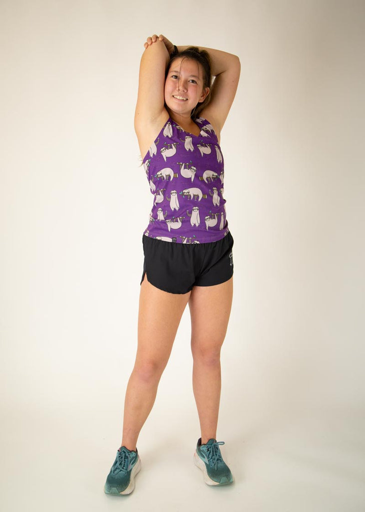 The model is a runner who is wearing Chicknlegs women's singlet in the sloths design, facing front while posing and stretching their arms.
