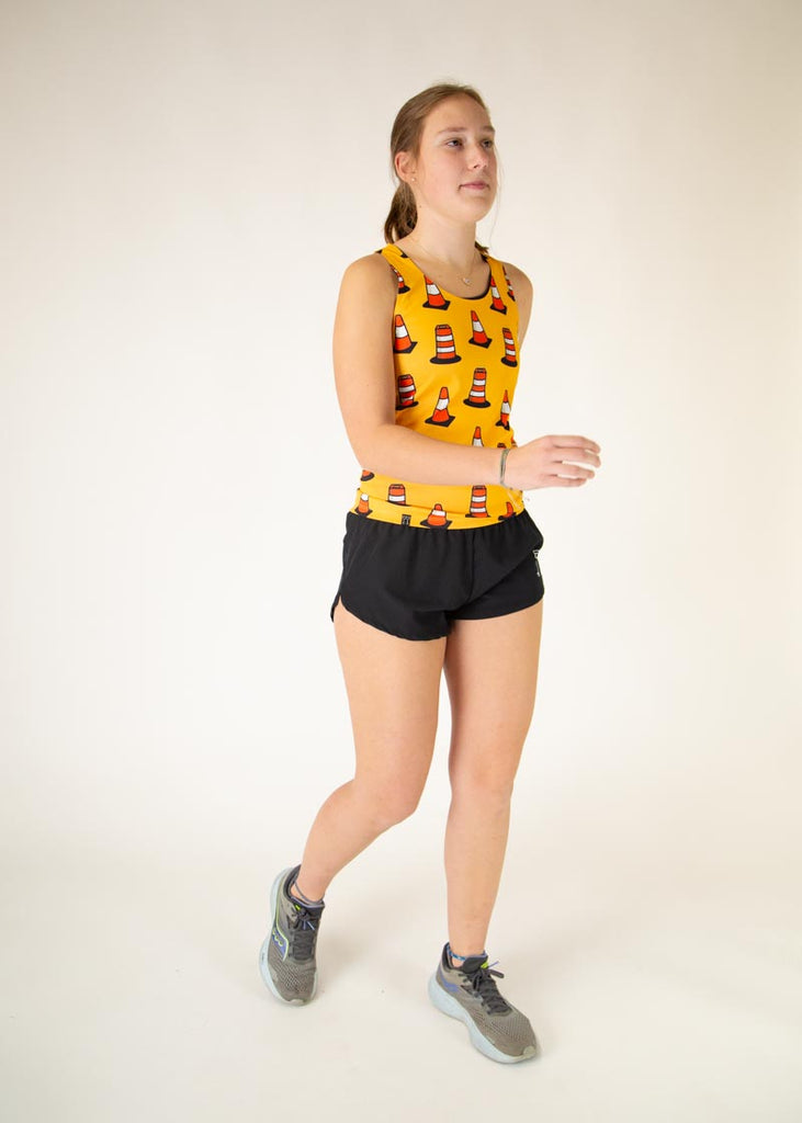 The model is a runner who is wearing Chicknlegs women's performance singlet in the traffic cones design, posing in a running position.