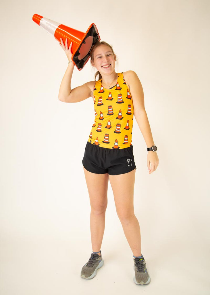 The model is a runner who is wearing Chicknlegs women's performance singlet in the traffic cones design, facing front while holding a traffic cone.