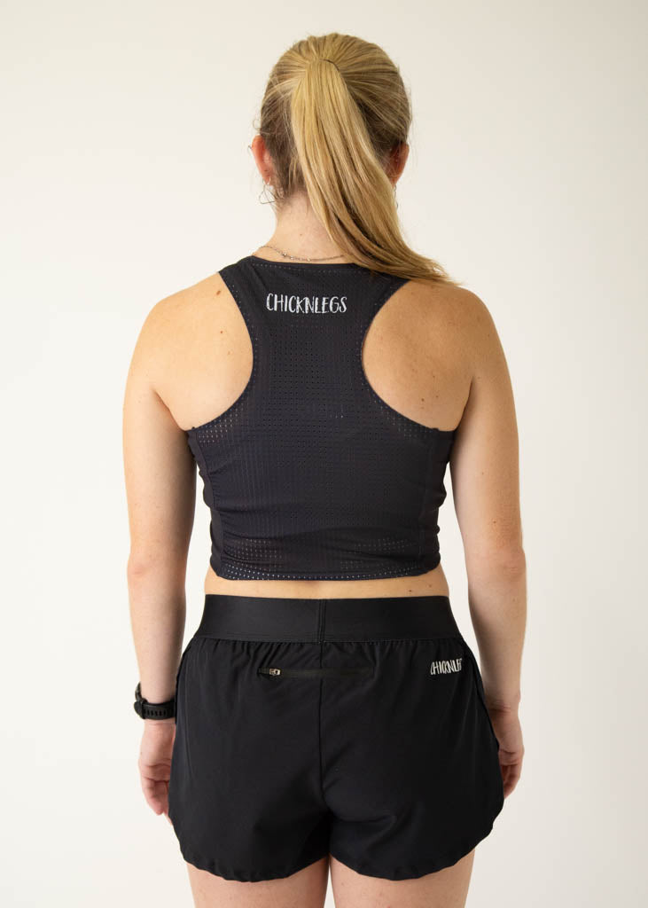 The model is a runner who is wearing Chicknlegs women's PWR crop top, in the black design, facing away from the camera to show the back of the crop top.
