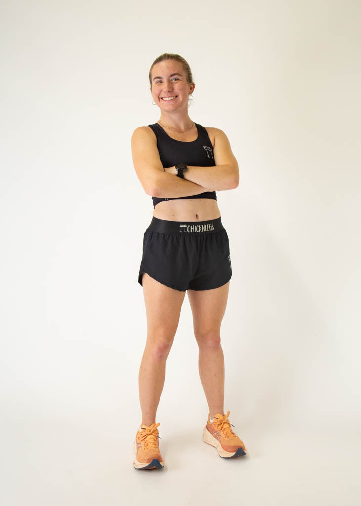 The model is a runner who is wearing Chicknlegs women's PWR crop top, in the black design, facing front while posing, crossing their arms.