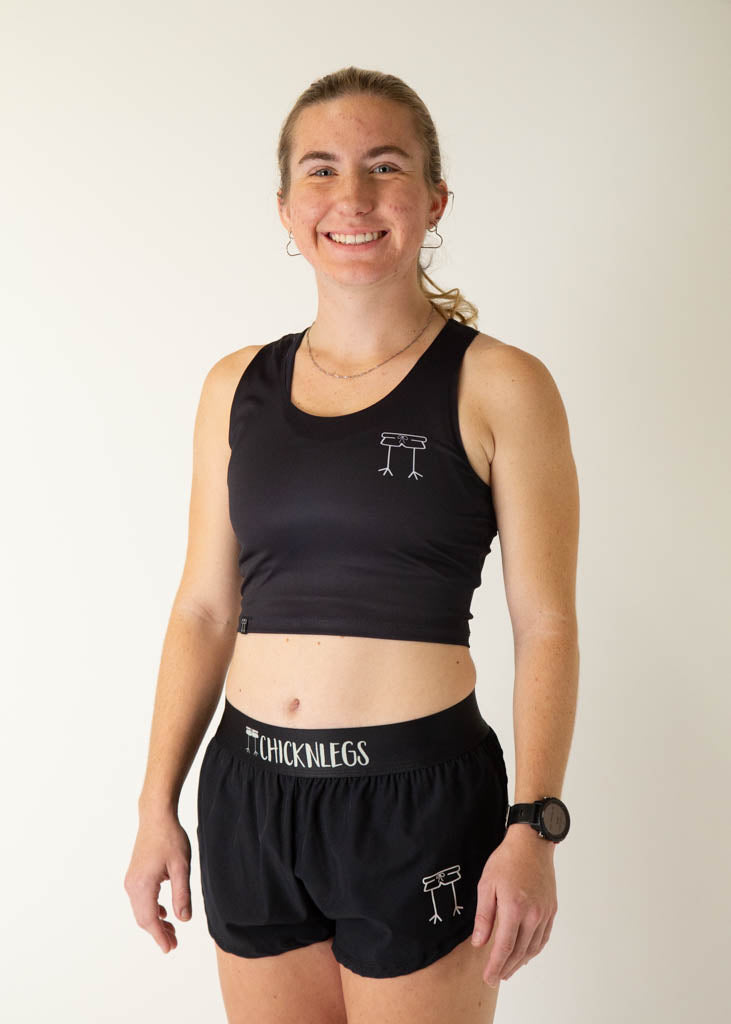 The model is a runner who is wearing Chicknlegs women's PWR crop top, in the black design, facing left.
