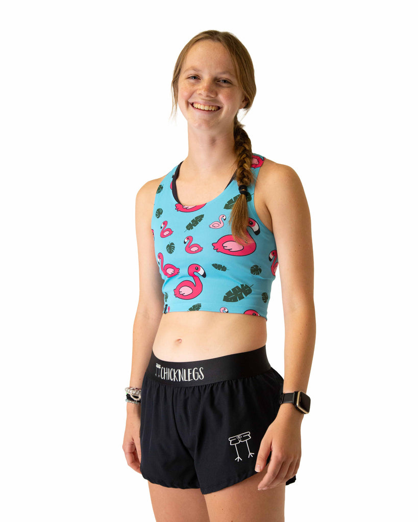 Runner is wearing ChicknLegs in the women's power crop top in the blue flamingo design. The material is lightweight and the print has pink flamingos on it with green leaves and a solid blue background.