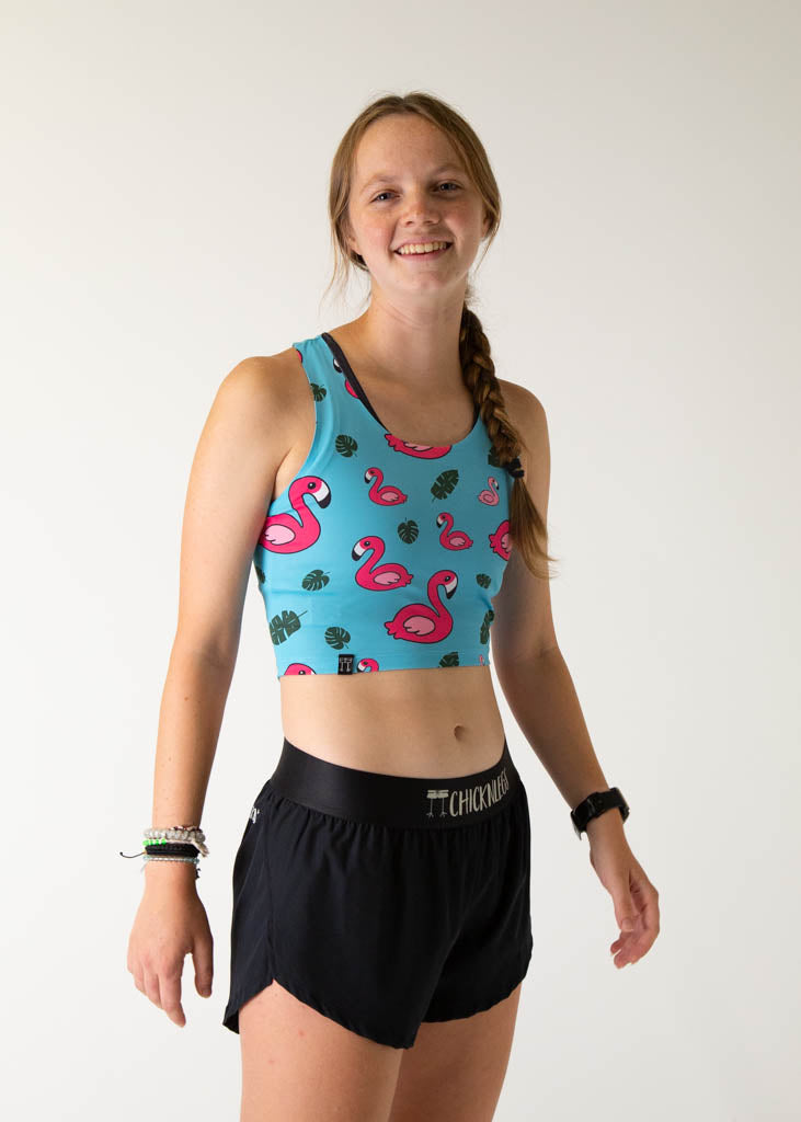 The model is a runner who is wearing Chicknlegs PWR crop top, in the blue flamingo design, facing right.