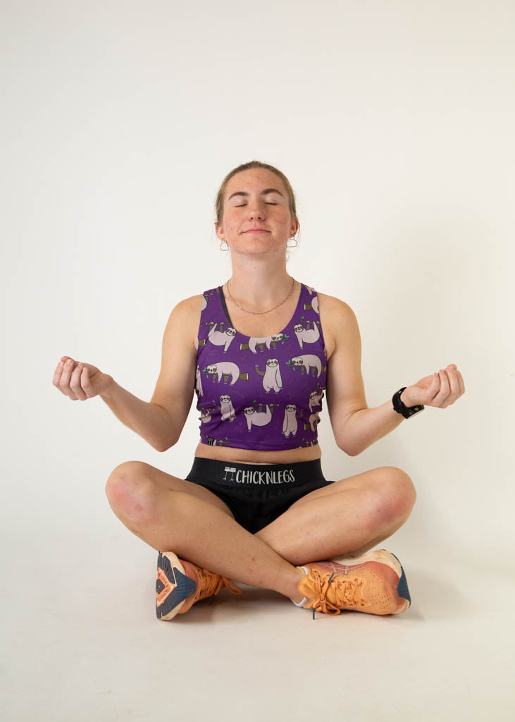 The model is a runner who is wearing Chicknlegs PWR crop top in the sloths design, facing front and posing while being in a zen state.