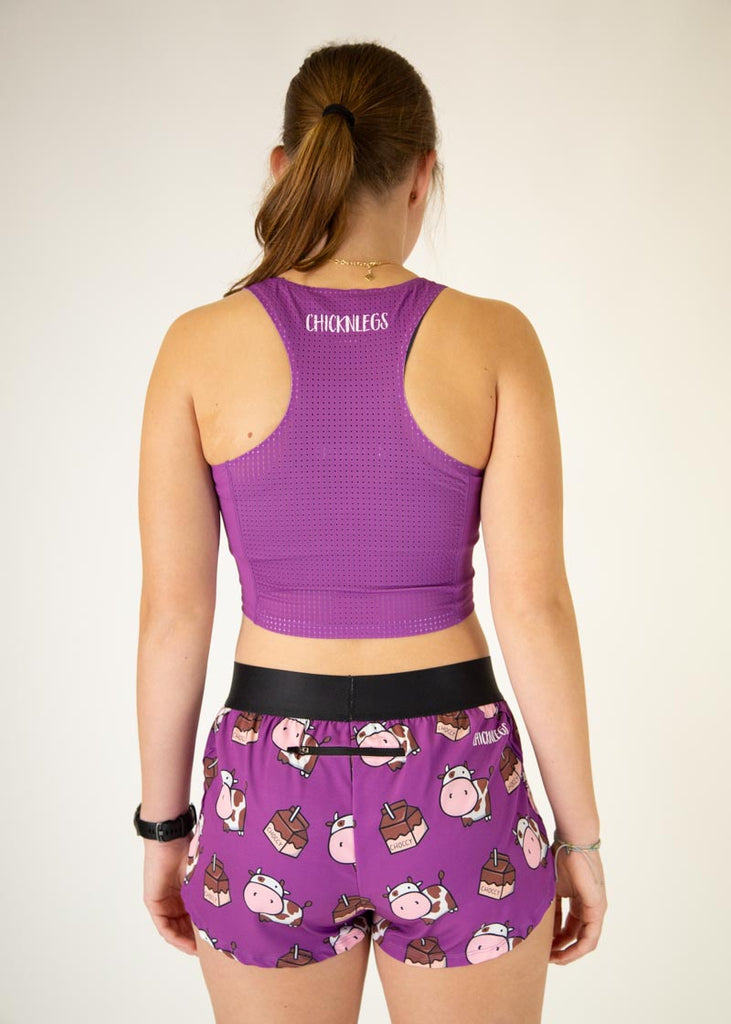 The model is a runner who is wearing Chicknlegs in women's pwr crop top in the deep purple design, matching with the choccy cow women's 1.5" split running shorts, facing away from the camera to show the back of the crop top.