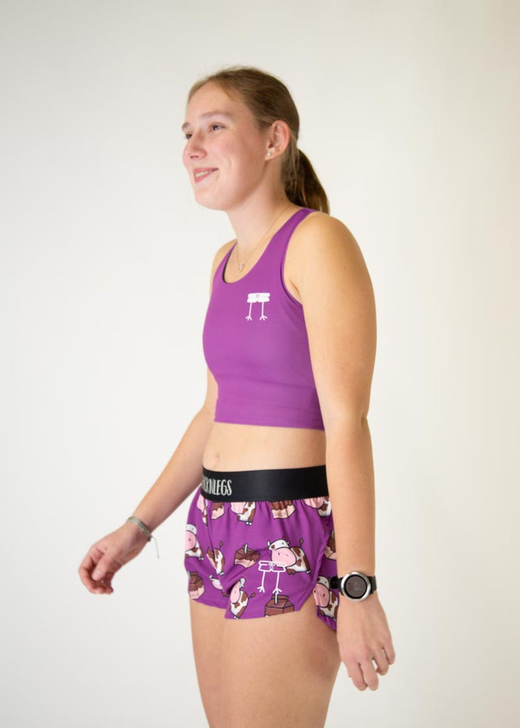 The model is a runner who is wearing Chicknlegs in women's pwr crop top in the deep purple design, matching with the choccy cow women's 1.5" split running shorts, facing left.