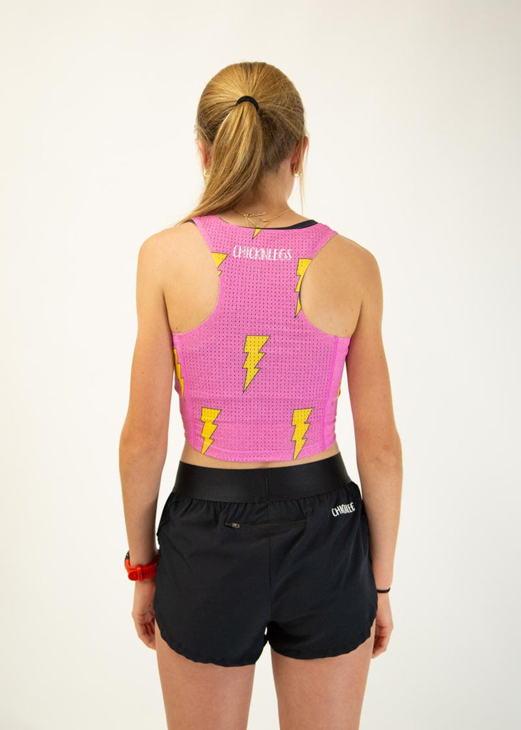 The model is a runner wearing Chicknlegs pwr crop top in the hot pink bolts design, facing away from the camera to show the back of the crop top.