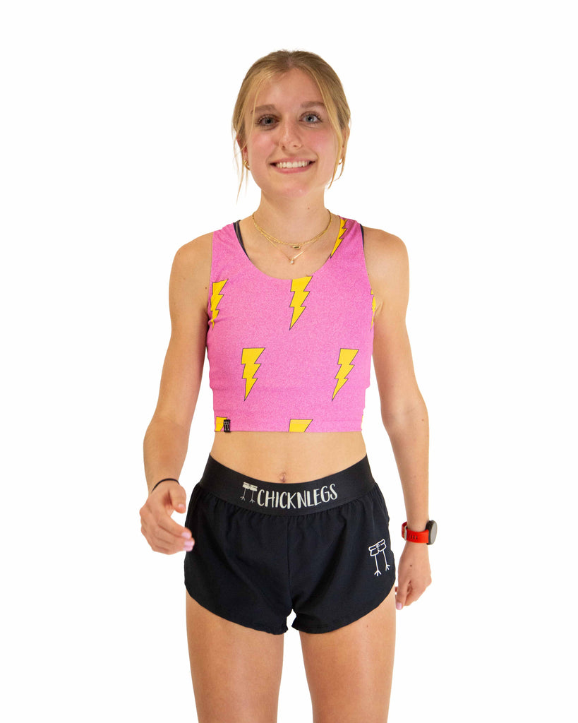 Runner is wearing ChicknLegs in the women's power crop top in the hot pink bolts design. The material is lightweight and the print has yellow lightning bolts and a hot pink background.