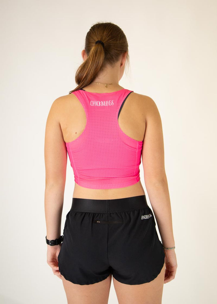 The model is a runner who is wearing Chicknlegs women's Neon Pink pwr crop top, facing away from the camera to show the back of the singlet.