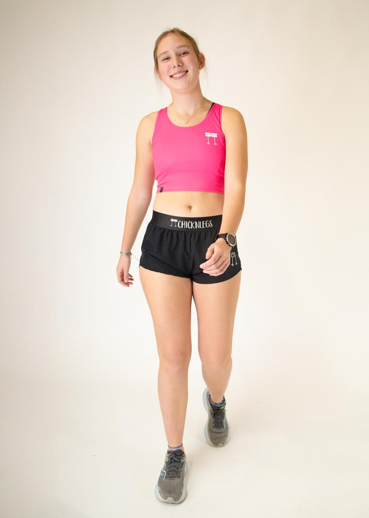 The model is a runner who is wearing Chicknlegs women's Neon Pink pwr crop top, facing front while posing in a walking position.