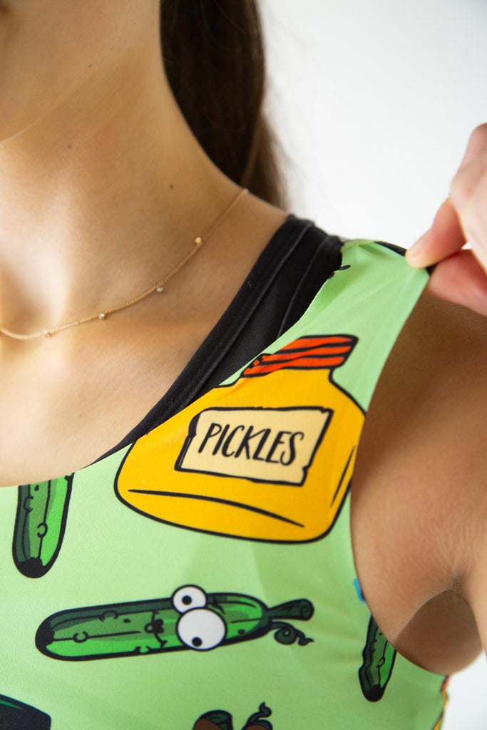 The model is a runner who is wearing Chicknlegs in the women's PWR crop top, in the pickles design, facing front while holding the side of the crop top to show the thin fabric in the photo.