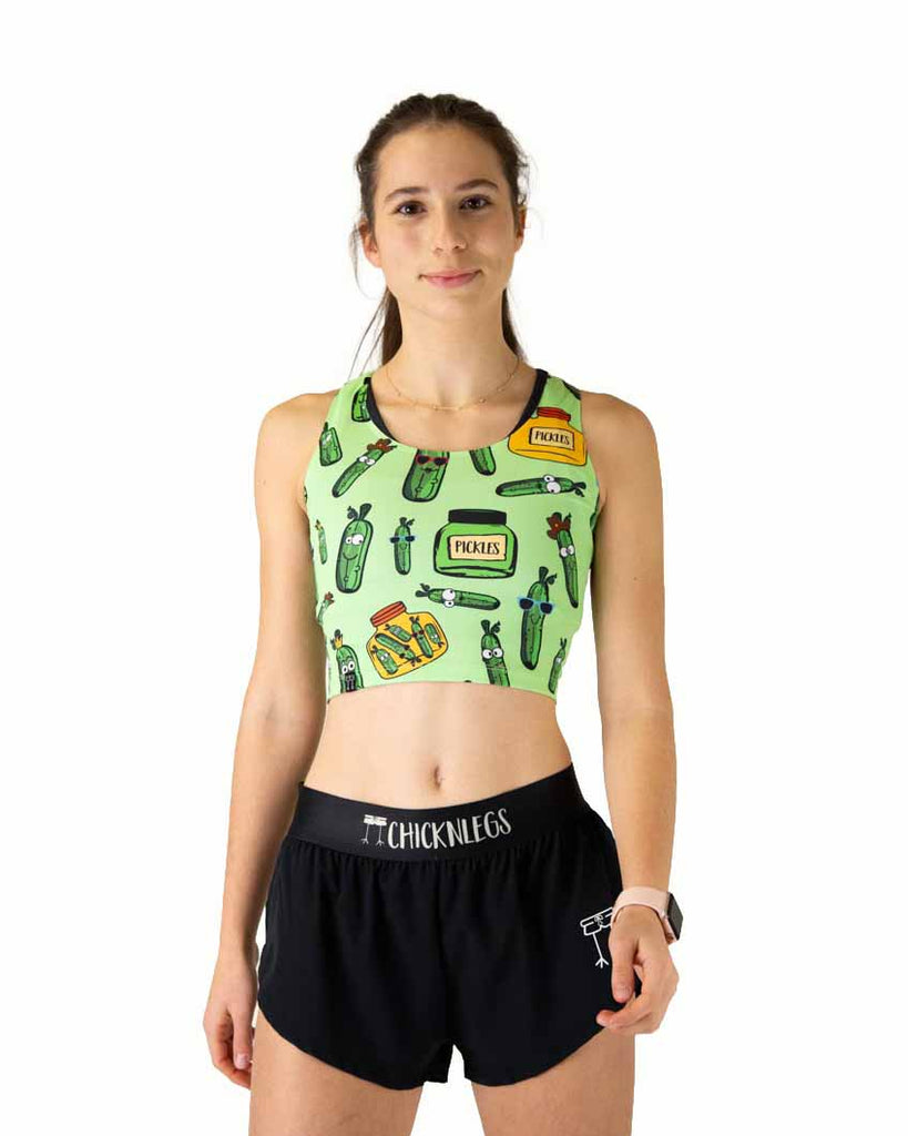 Runner is wearing ChicknLegs in the women's power crop top in the pickles design. The material is lightweight and the print has pickles all over it with yellow and green jars.