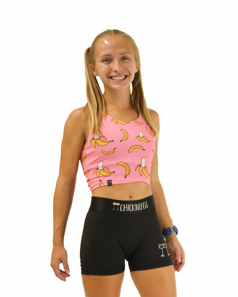 Runner is wearing ChicknLegs in the women's power crop top in the pink bananas design. The material is lightweight and the print has yellow bananas and a pink background.