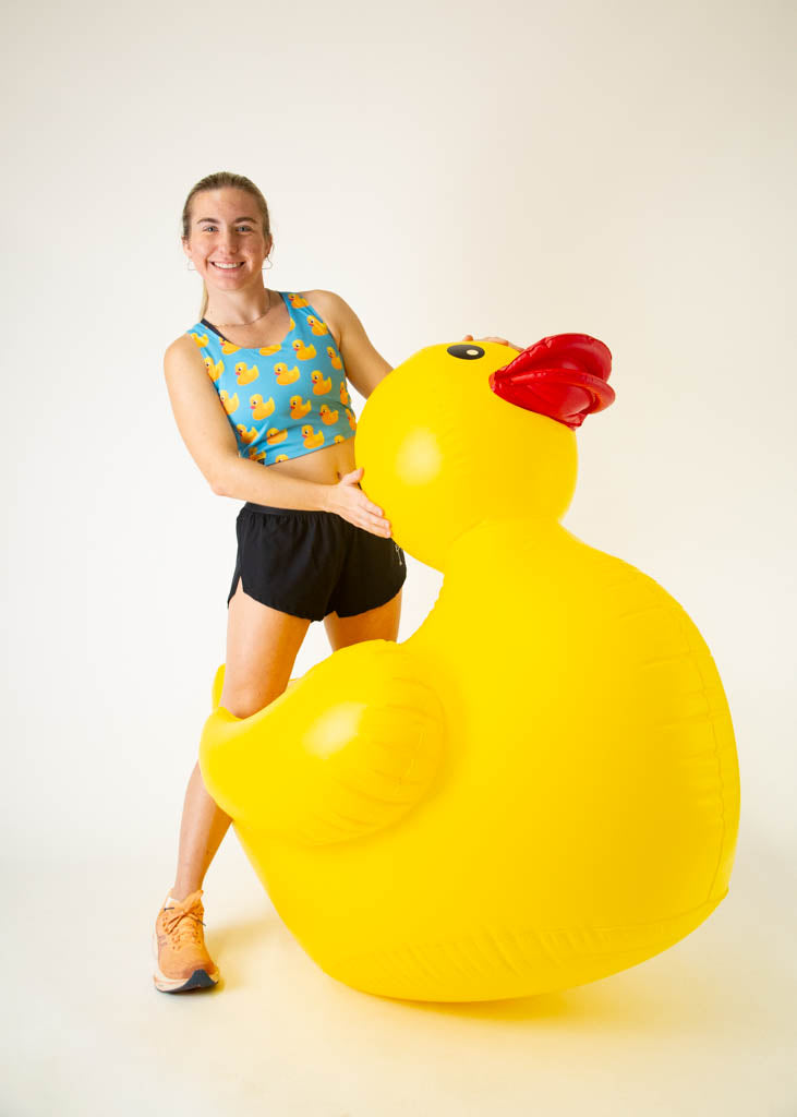 The model is a runner who is wearing Chicknlegs PWR crop top, in the rubber ducky design, facing front while posing with a huge giant rubber ducky