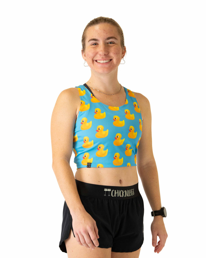Runner is wearing ChicknLegs in the women's power crop top in the rubber duckys design. The material is lightweight and the print has yellow rubber ducks on it with a blue background.