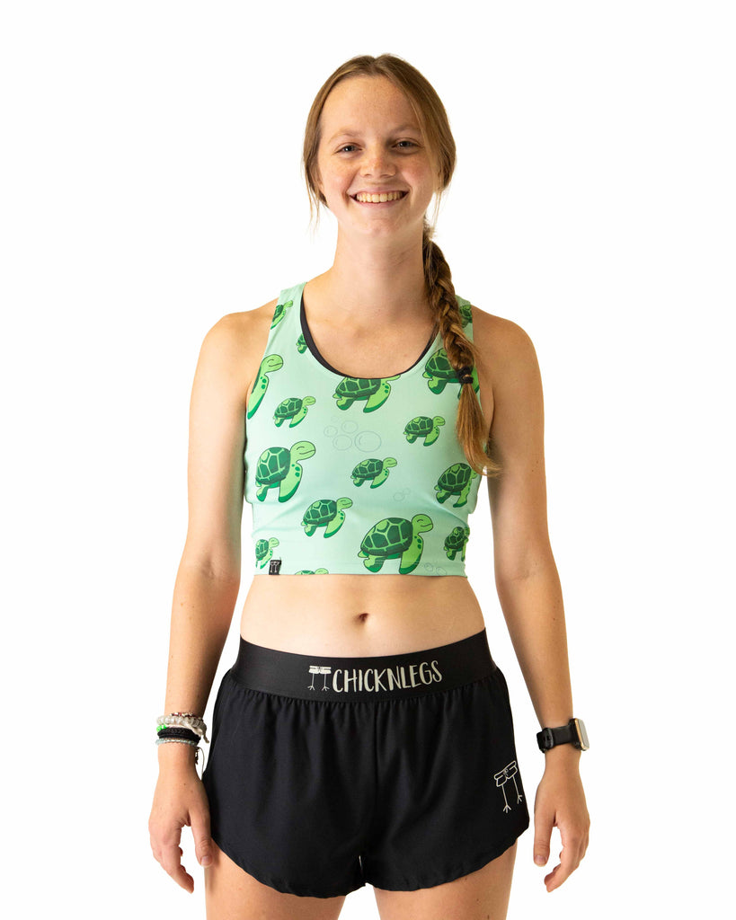 Runner is wearing ChicknLegs in the women's power crop top in the sea turtles design. The material is lightweight and the print has bubbles and green turtles on it with a light green solid background.