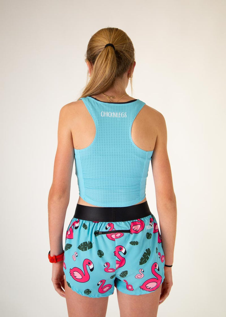 The model is a runner who is wearing Chicknlegs women's pwr crop top in the sky blue design, facing front. The model is matching the pwr crop with the women's 1.5" split running shorts in the blue flamingo design. The model is facing away from the camera to show the back of the crop.