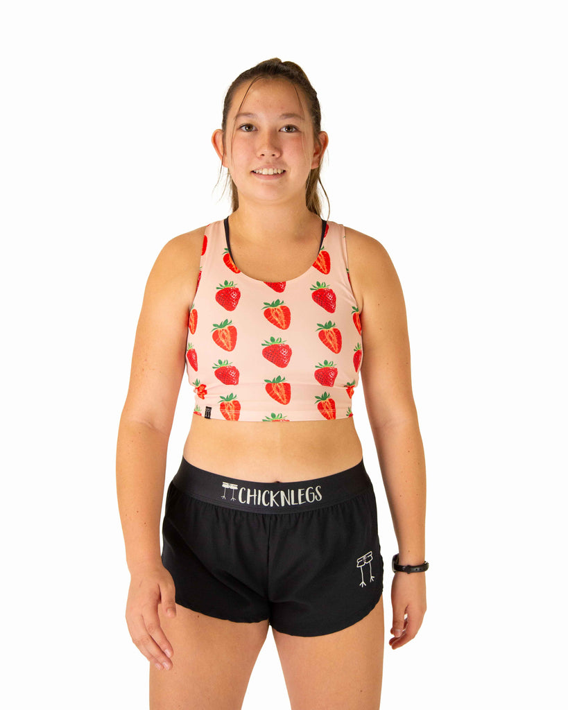 Runner is wearing ChicknLegs in the women's power crop top in the strawberry szn design. The material is lightweight and the print has red and pink strawberries over it.