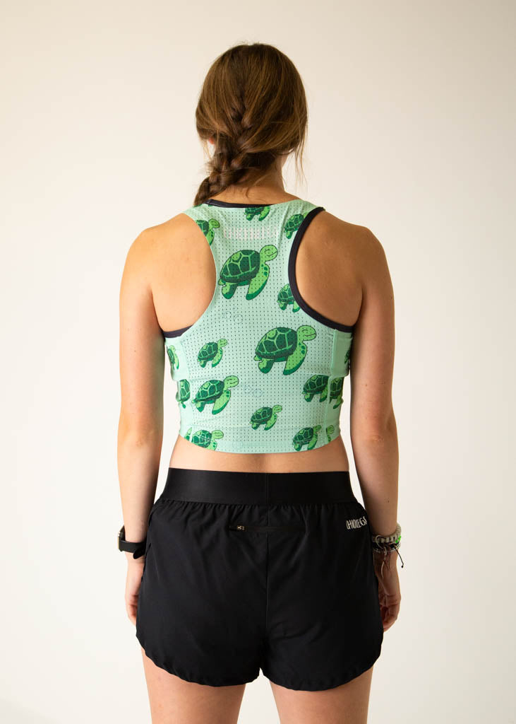 The model is a runner who is wearing Chicknlegs PWR crop top in the turtles design, facing away from the camera to show the back of the crop top.