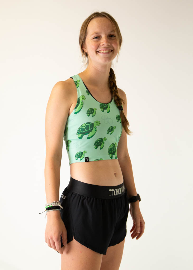 The model is a runner who is wearing Chicknlegs PWR crop top in the turtles design, facing right.