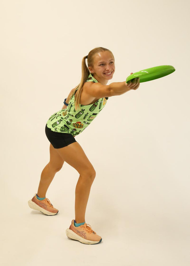 Model is wearing Chicknlegs women's singlet in the pickles design posing with a green frisbee. 