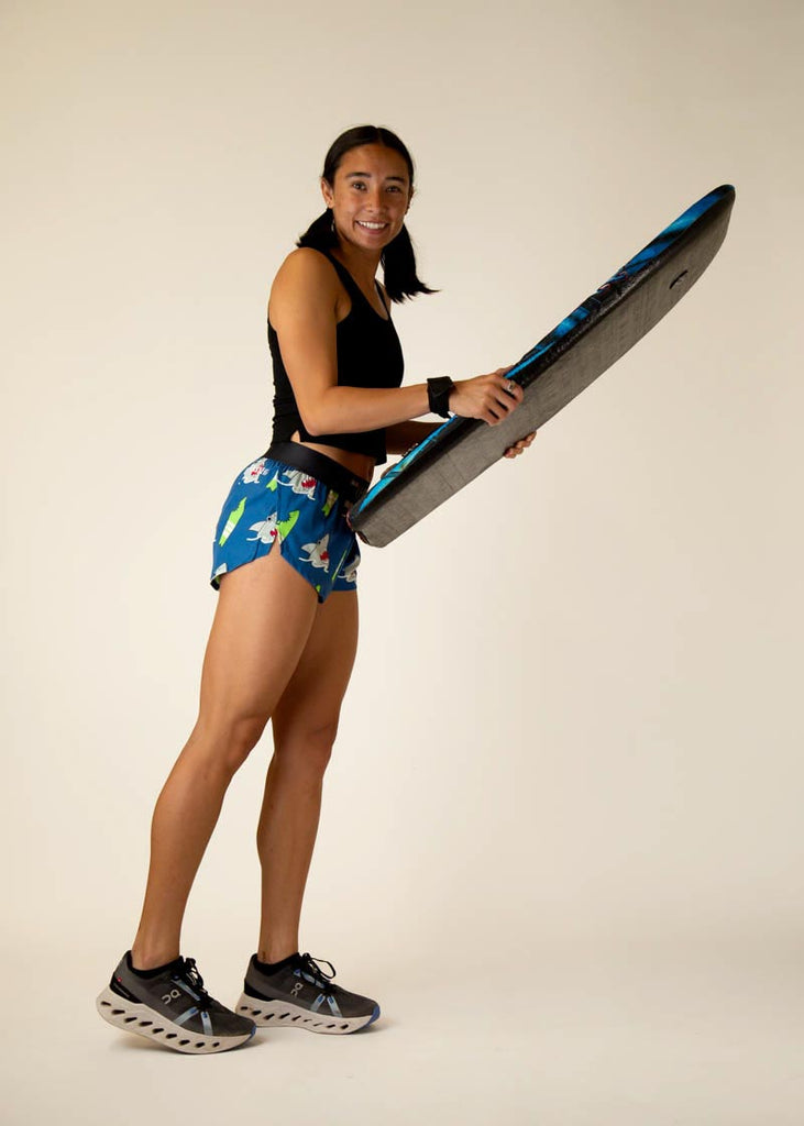 Full body view of the women's sharks 1.5 inch running shorts holding surf board.