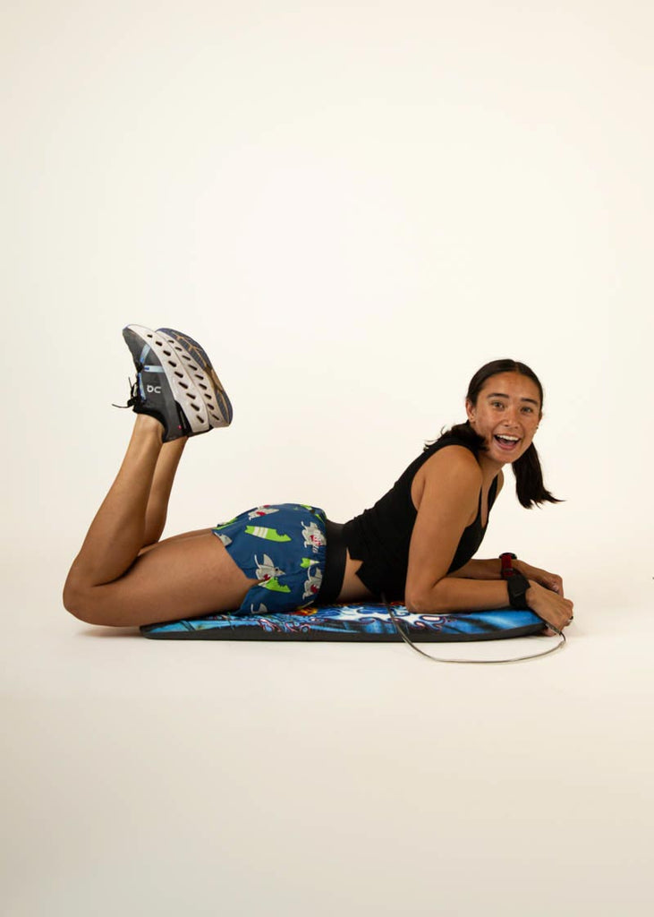 Full body view of the women's sharks 1.5 inch running shorts on surf board.
