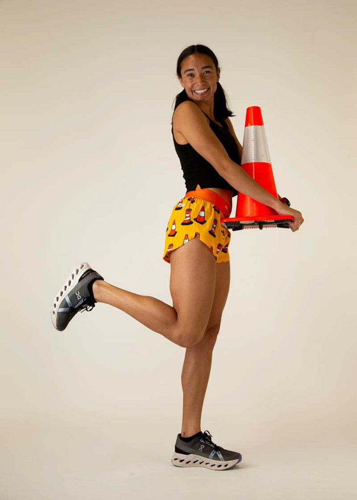 Full body view of the women's traffic cones 1.5 inch split running shorts holding a traffic cone while standing.