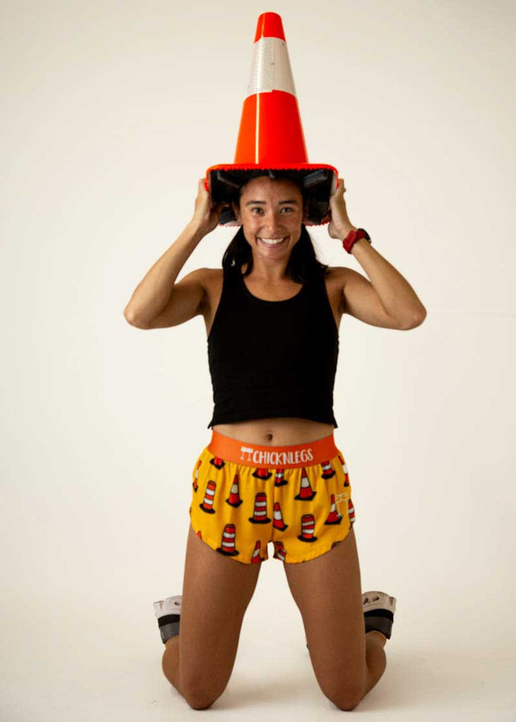 Full body view of the women's traffic cones 1.5 inch split running shorts holding a traffic cone.