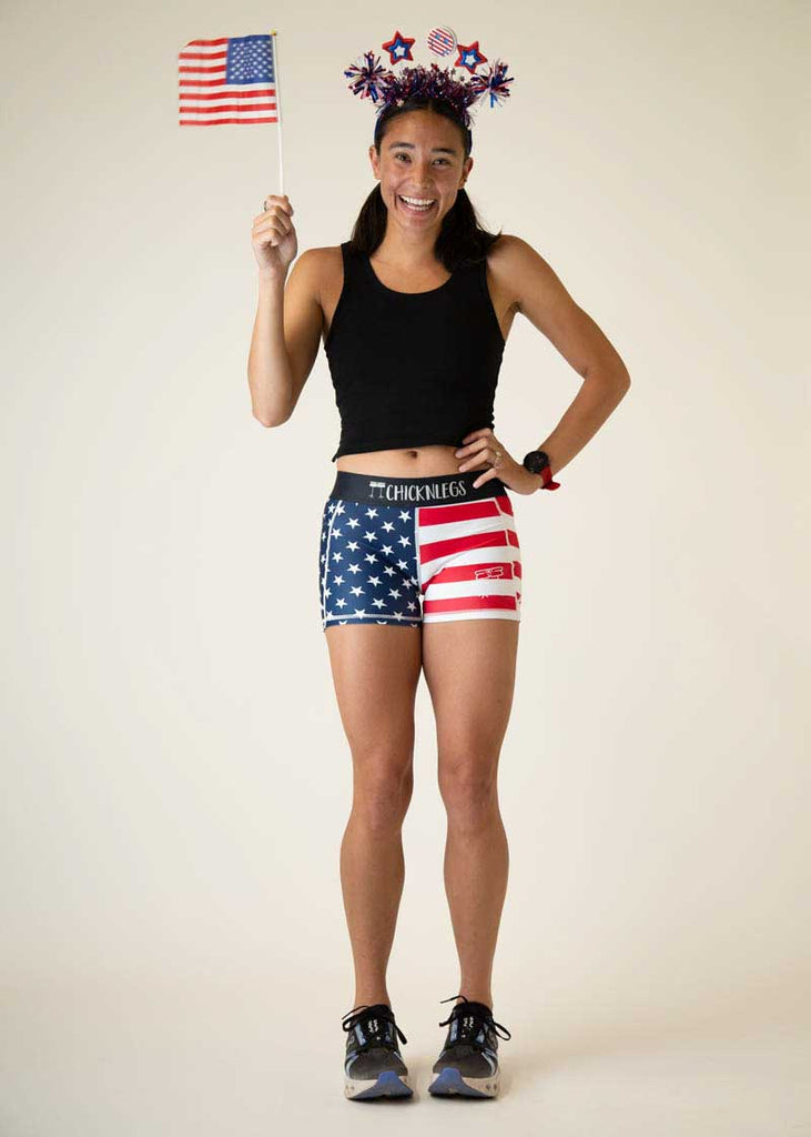 Full body view of the women's 3 inch USA compression running shorts from ChicknLegs holding a mini flag.