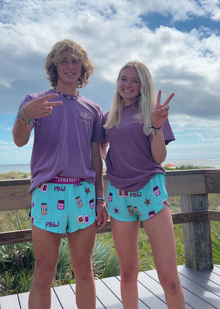 Two models are shown wearing Chicknleg's men's 2 inch split running short and women's 1.5" split running short in the PB&J design that includes PB&J sandwiches, peanut butter, jelly on a light blue background, facing front.