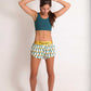 ChicknLegs women's trippy pineapples 1.5" split running shorts full body shot with green sports bra and fixing hair.