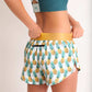ChicknLegs women's trippy pineapples 1.5" split running shorts back view holding waistband and showcasing the zipper pocket.