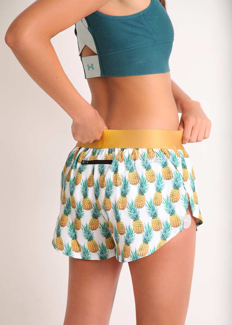 ChicknLegs women's trippy pineapples 1.5" split running shorts back view holding waistband and showcasing the zipper pocket.