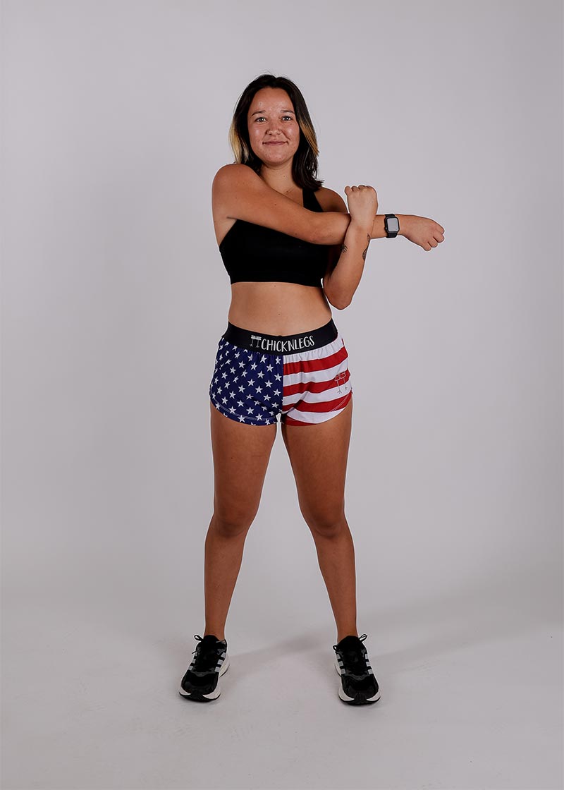 Full body view of model stretching in the ChicknLegs women's USA split running shorts.